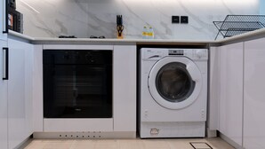 Uma cozinha compacta com forno embutido e máquina de lavar frontal, armários brancos e painel de parede de mármore.