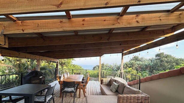 Un espacio al aire libre cubierto con una terraza de madera, una mesa con sillas, un sofá y una parrilla.