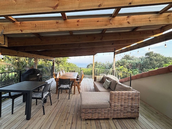 A covered outdoor area with a wooden deck, a table with chairs, a sofa, and a grill.