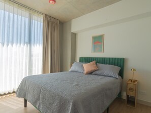 Une chambre à coucher avec un lit, des rideaux, une table de chevet et une lampe fixée au mur.