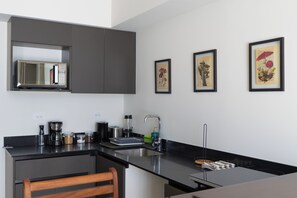 Une cuisine moderne équipée d’un four à micro-ondes, d’une machine à café et d’un évier. Des tableaux encadrés ornent le mur.