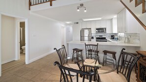A spacious kitchen with white cabinets, a central island, and a dining area with four chairs. - Lei Lani Mini Tower 315N by Liquid Life (Orange Beach)