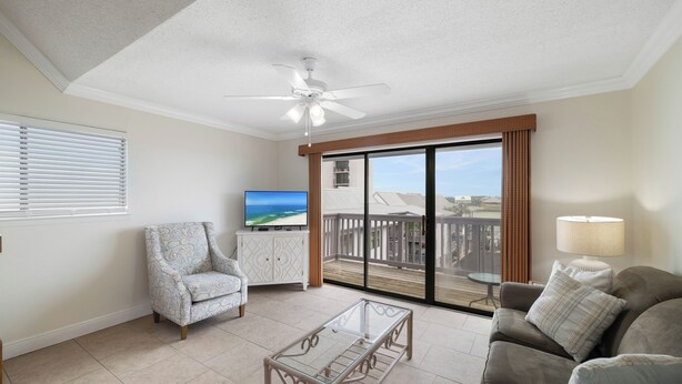 A living room with a television, a ceiling fan, a glass coffee table, a sofa, and a view of a balcony with a railing. - Lei Lani Mini Tower 315N by Liquid Life (Orange Beach)