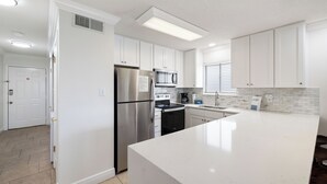 A modern kitchen with white cabinetry, stainless steel appliances, and a large island. - Lei Lani Mini Tower 315N by Liquid Life (Orange Beach)