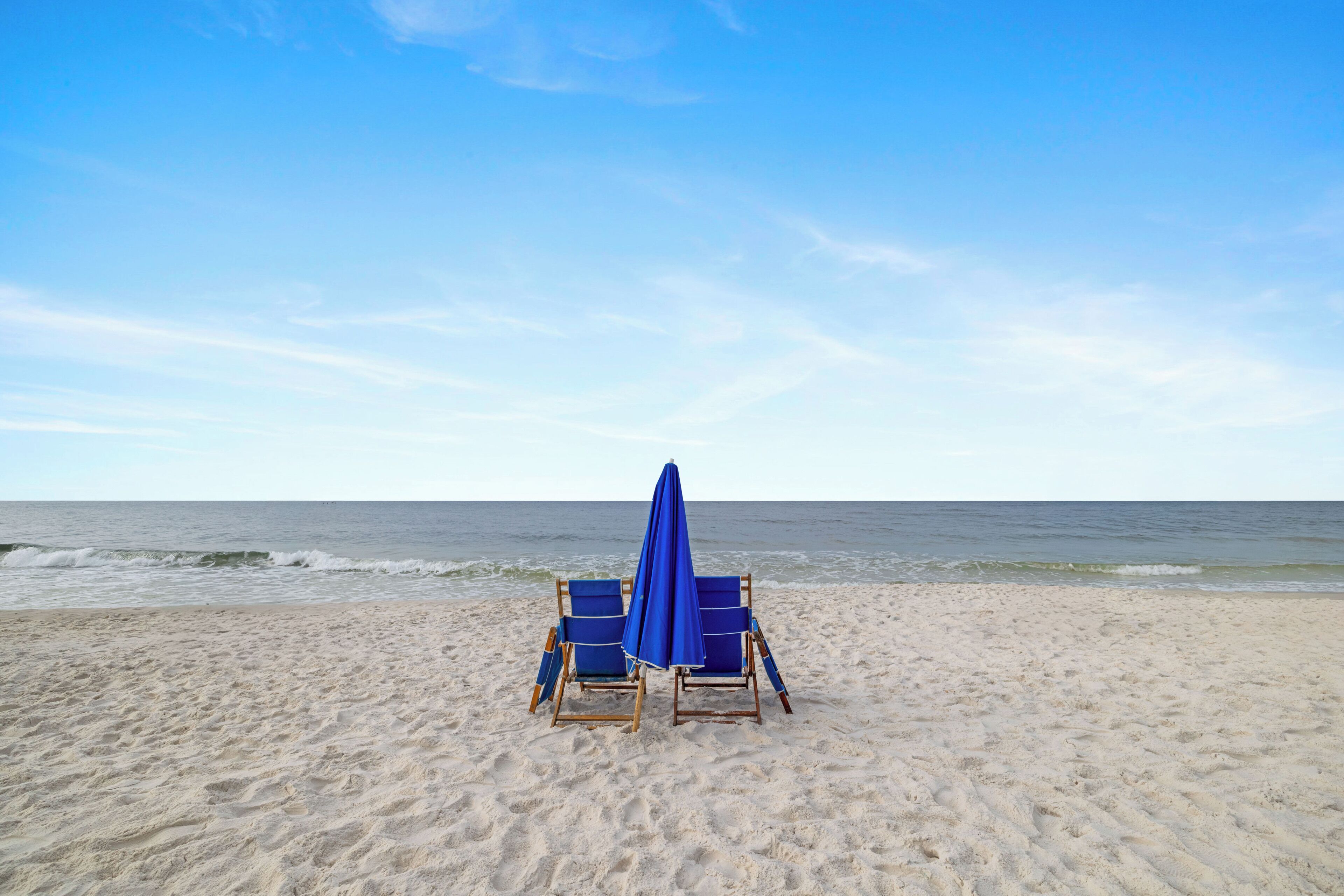 Ein Strand mit zwei blauen Liegen und einem blauen Sonnenschirm.