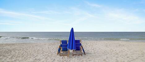 Ein Strand mit zwei blauen Liegen und einem blauen Sonnenschirm.