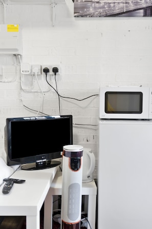 Pared de ladrillo blanco con una televisión, una cafetera blanca y un microondas blanco sobre una encimera.