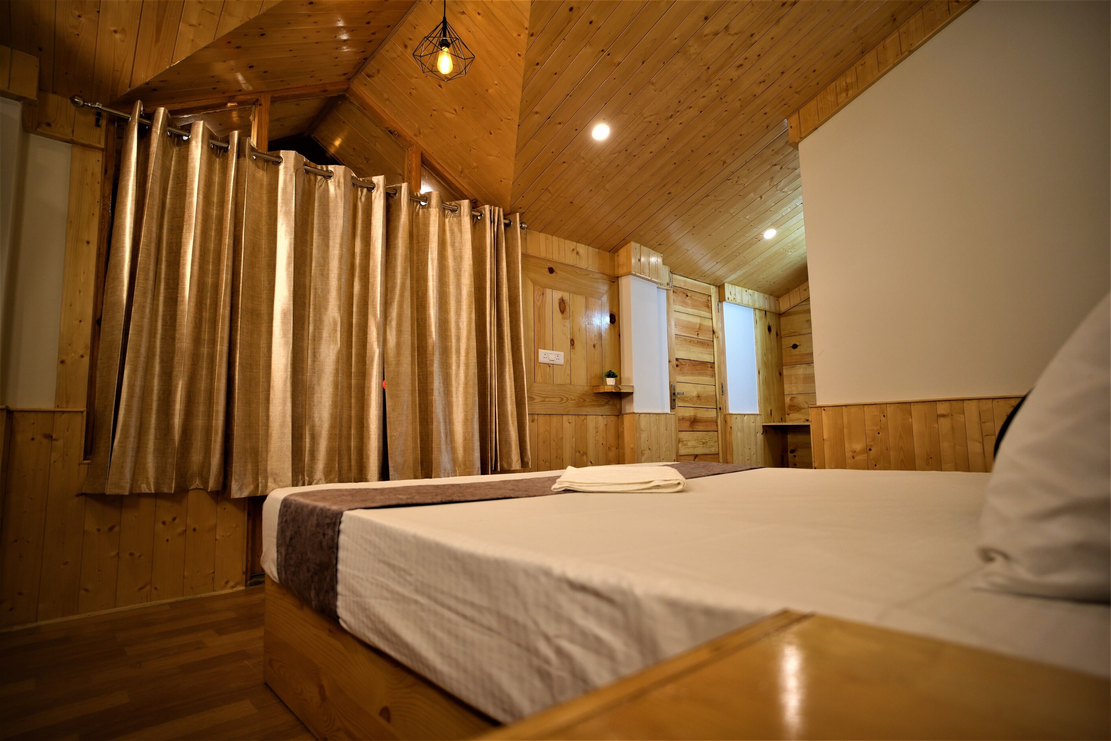 A wooden cabin bedroom with a bed, curtains, and a hanging light fixture.