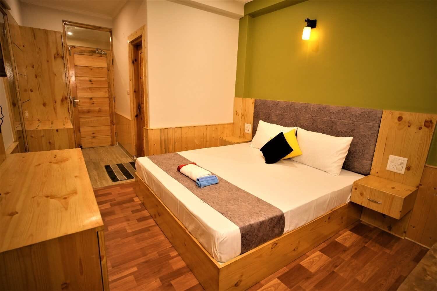 Une pièce en bois comprenant un lit, une table de chevet, une commode, une armoire en bois et un luminaire fixé au mur.