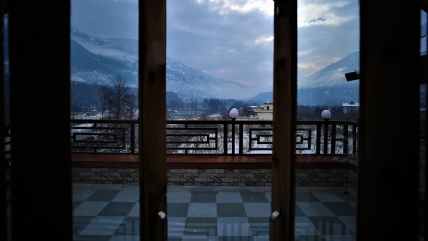 A balcony with a view of snow-covered mountains and a cloudy sky. - Mountainshack Riverside Stay & Cafe (Kullu)