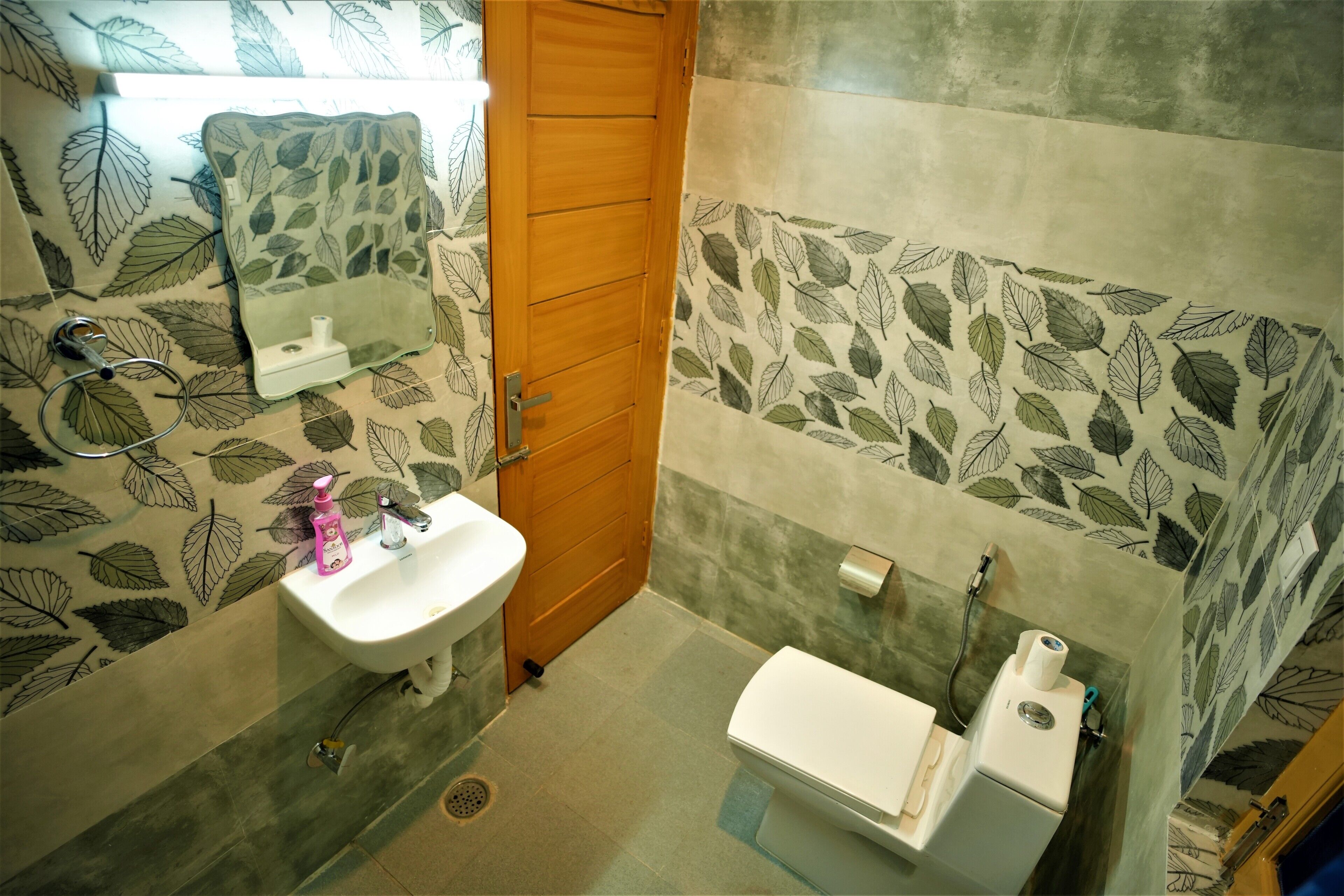 Ein Badezimmer mit Holztür, weißem Waschbecken, Toilette und einem Spiegel mit Wandverkleidung in Blattform.