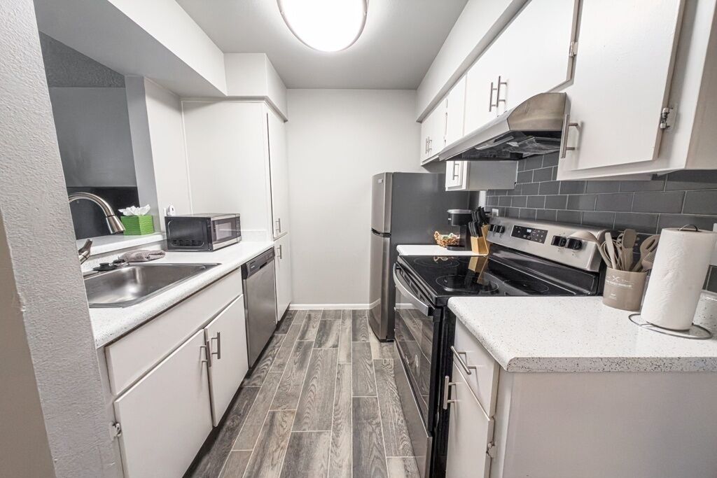 A compact kitchen with white cabinets, a black refrigerator, a stove, and a microwave.