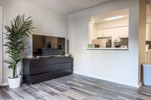 Een moderne woonkamer met een flatscreen televisie, een donkere houten dressoir en een grote kamerplant.
