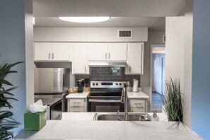 A compact kitchen with white cabinets, a stainless steel refrigerator, a built-in oven, and a countertop with a sink. - Pool -Gym- Great for Mid/Long Stays (Mesa)