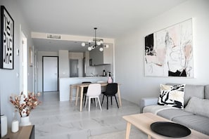 Ein modernes Wohnzimmer mit einer Couch, einem Esstisch mit Stühlen, einer Küchenzeile und einem großen abstrakten Gemälde an der Wand.