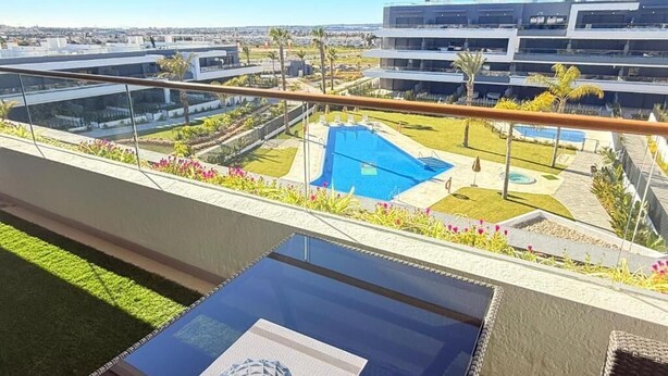A rooftop pool with a glass balustrade, a clear view of the cityscape, and a modern building in the background. - Apartment Lagoons Village Torrevieja (Torrevieja)