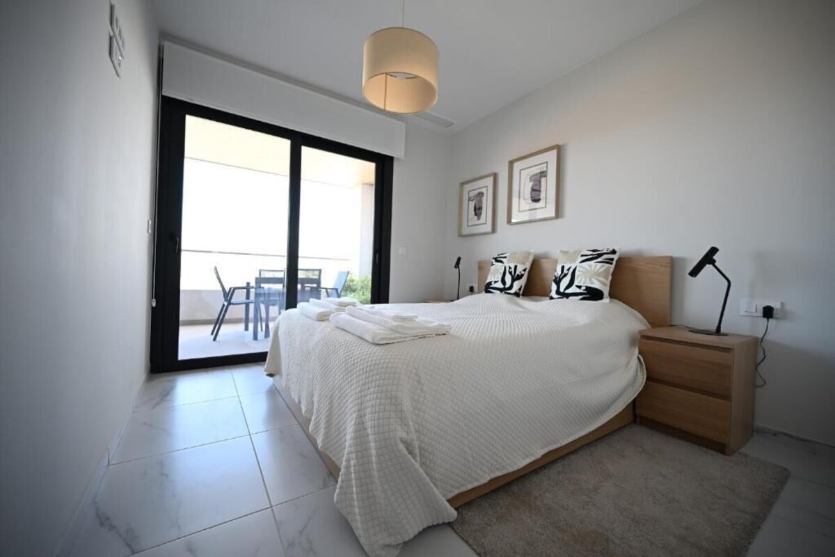 A bedroom with a bed, a nightstand, a lamp, and a sliding glass door leading to a balcony.