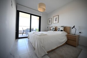 Un dormitorio con cama, mesita de noche, lámpara y puerta corrediza de vidrio que da a un balcón.