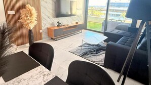 A modern living room with a flat-screen TV, a sofa, a coffee table, and a dining area with a marble table. - Apartment Lagoons Village Torrevieja (Torrevieja)