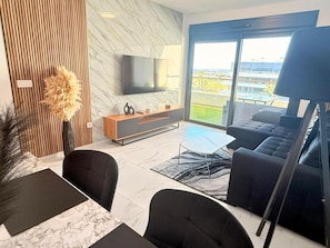 Una sala de estar moderna con un televisor de pantalla plana, un sofá, una mesa de centro y un comedor con una mesa de mármol.