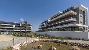 A modern multi-story hotel with balconies, a landscaped garden, and a pool area. - Apartment Lagoons Village Torrevieja (Torrevieja)