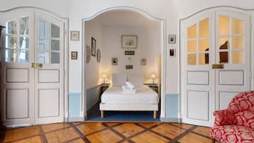 A hotel room with a bed, two bedside tables, a red patterned chair, and a wooden parquet floor.