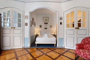 A hotel room with a bed, two bedside tables, a red patterned chair, and a wooden parquet floor. - Château with Private Park – Gîte du Tilleul – Exceptional Setting (Tournon)