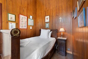 A neatly made bed in a room with wooden paneling, a nightstand with a lamp, and several framed pictures on the wall. - Château with Private Park – Gîte du Tilleul – Exceptional Setting (Tournon)
