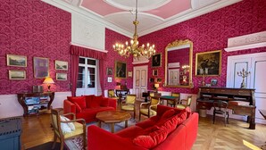 Una habitación con sofá rojo, muebles de madera, candelabro y piano.