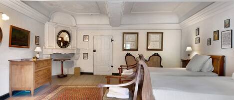 Une chambre traditionnelle avec un lit, deux chaises, une commode en bois, une table ronde et un miroir.
