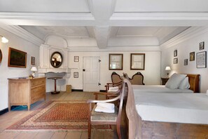 A traditional room with a bed, two chairs, a wooden dresser, a round table, and a mirror.