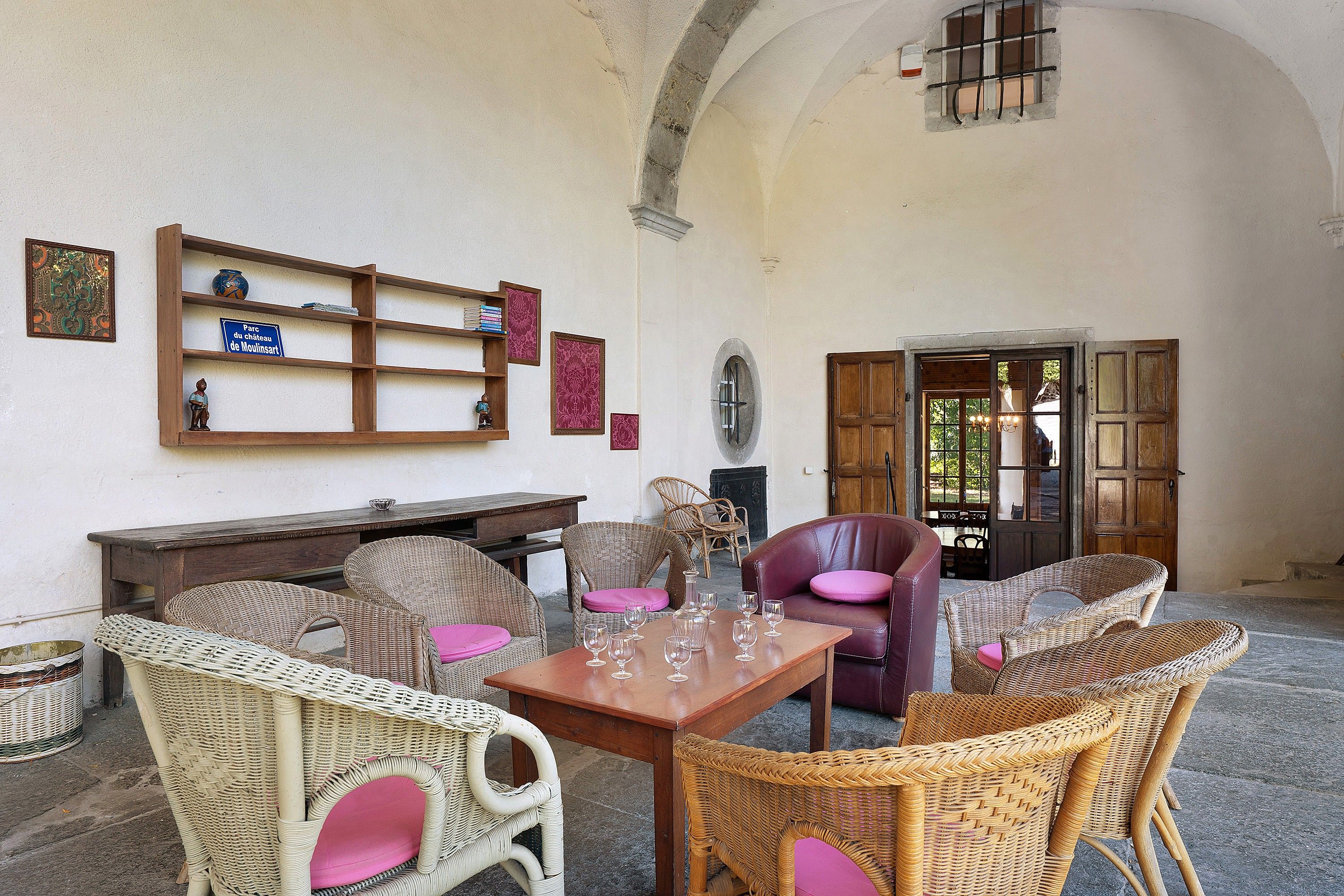 Une pièce meublée de meubles en osier, avec une table en bois et des verres à vin, et une porte donnant sur l’extérieur.