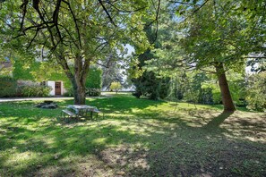 A grassy outdoor area with a picnic table and benches, surrounded by trees and a building in the background. - Château with Private Park – Gîte du Tilleul – Exceptional Setting (Tournon)