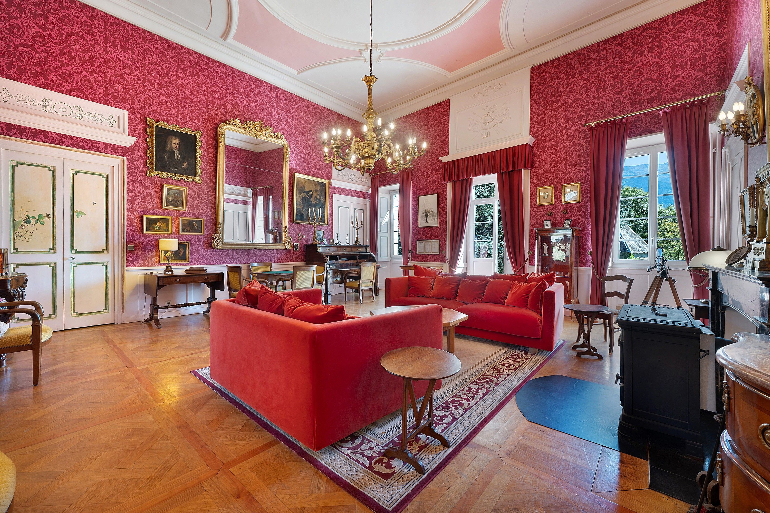 Ein Zimmer mit einem roten Sofa, Holzboden, einer Chandelüster und einem großen Spiegel.