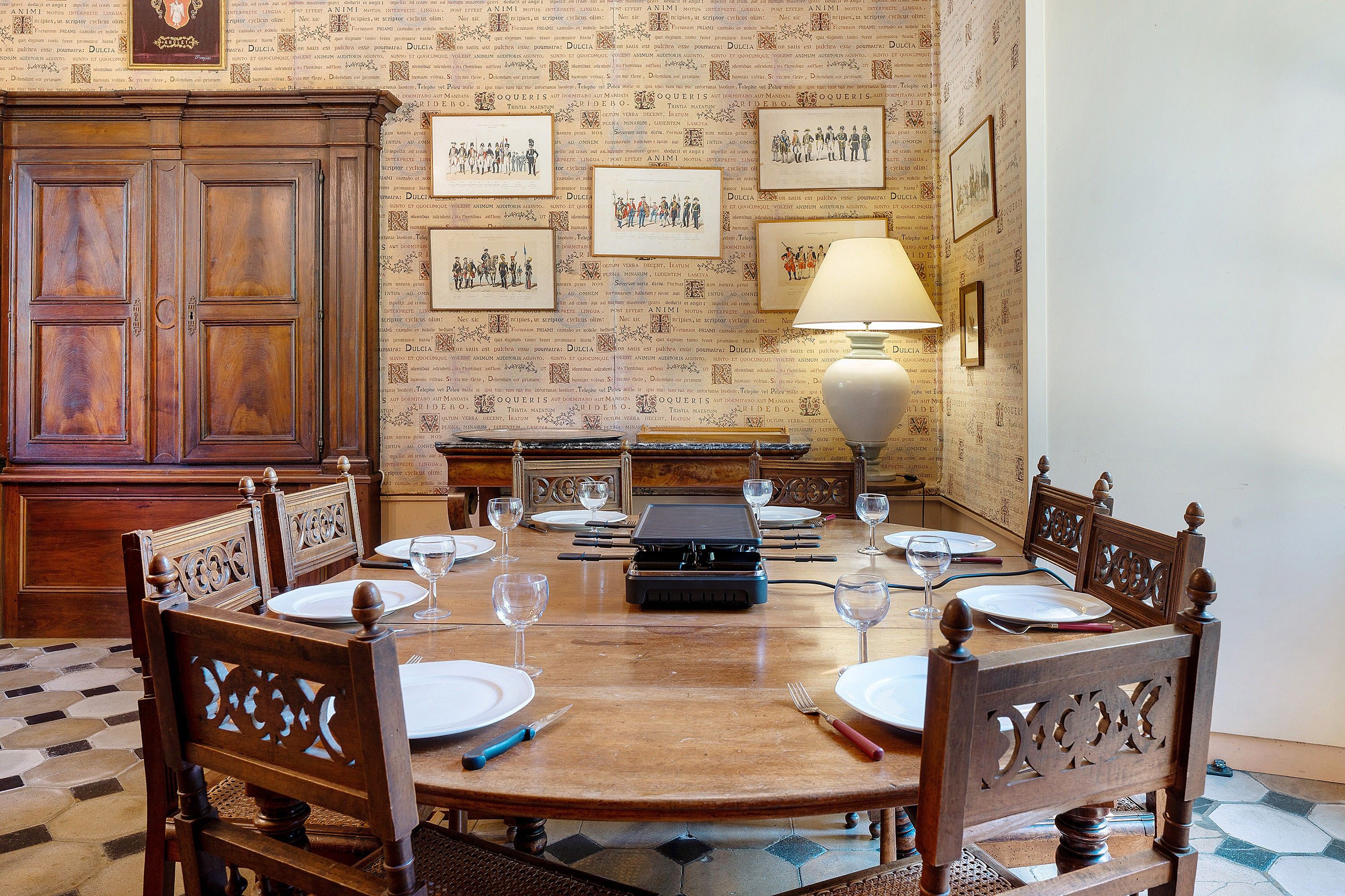 A dining area with a wooden table set for six, surrounded by ornate chairs, a vintage radio, and a lamp.