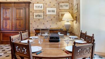 A dining area with a wooden table set for six, surrounded by ornate chairs, a vintage radio, and a lamp.