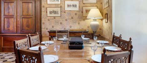 Un coin repas avec une table en bois dressée pour six personnes, entourée de chaises décoratives, d’une radio ancienne et d’une lampe.