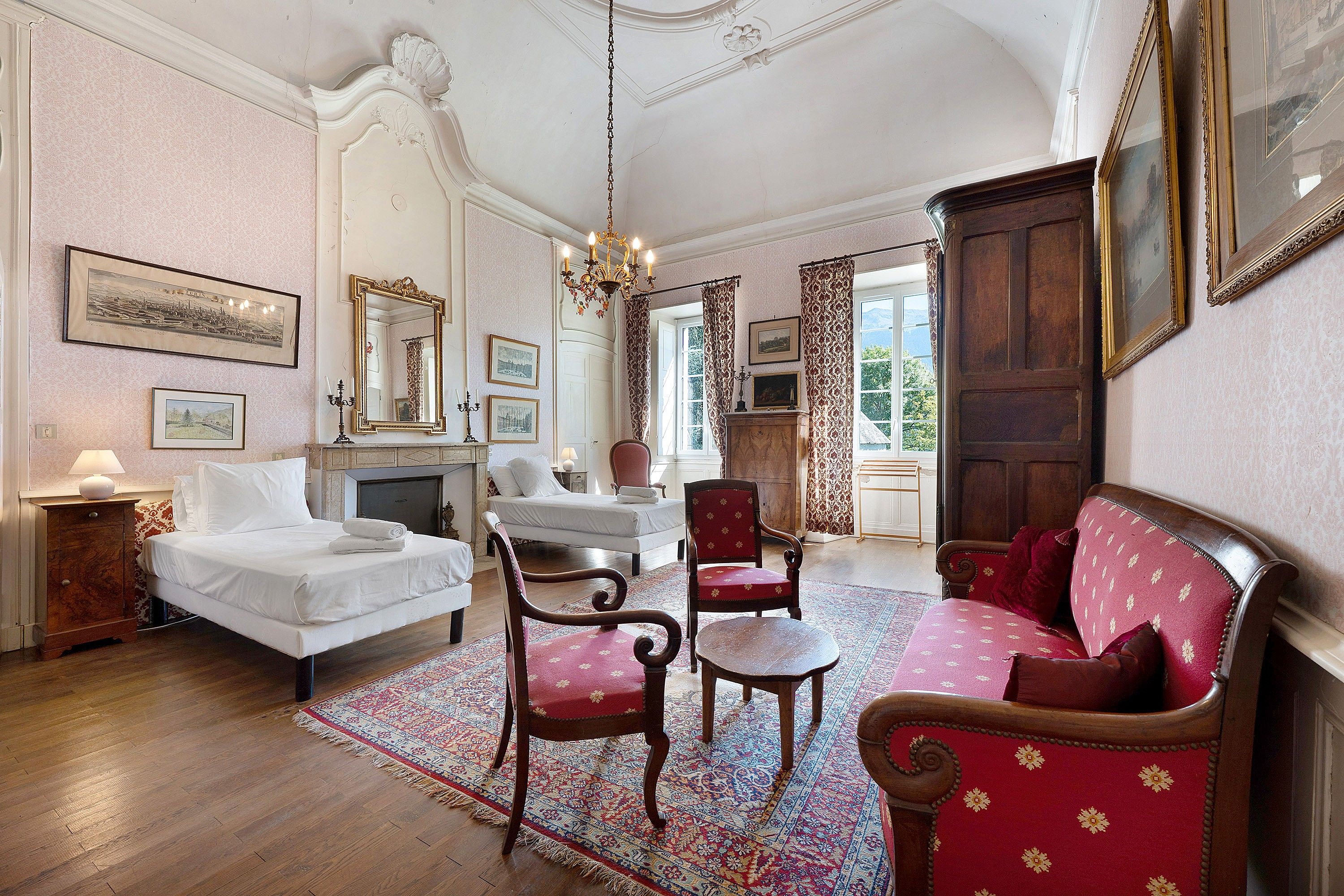 Une chambre classique comprenant un lit, deux fauteuils, un canapé, une cheminée et un grand miroir.
