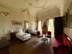 A hotel room with two beds, a sofa, a chair, a fireplace, and a large window with curtains.