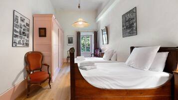 A hotel room with a wooden bed, a chair, a hanging light fixture, and framed pictures on the walls.