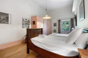 A bedroom with a wooden bed, a wardrobe, a hanging light fixture, and a window with curtains. - Château with Private Park – Gîte du Tilleul – Exceptional Setting (Tournon)
