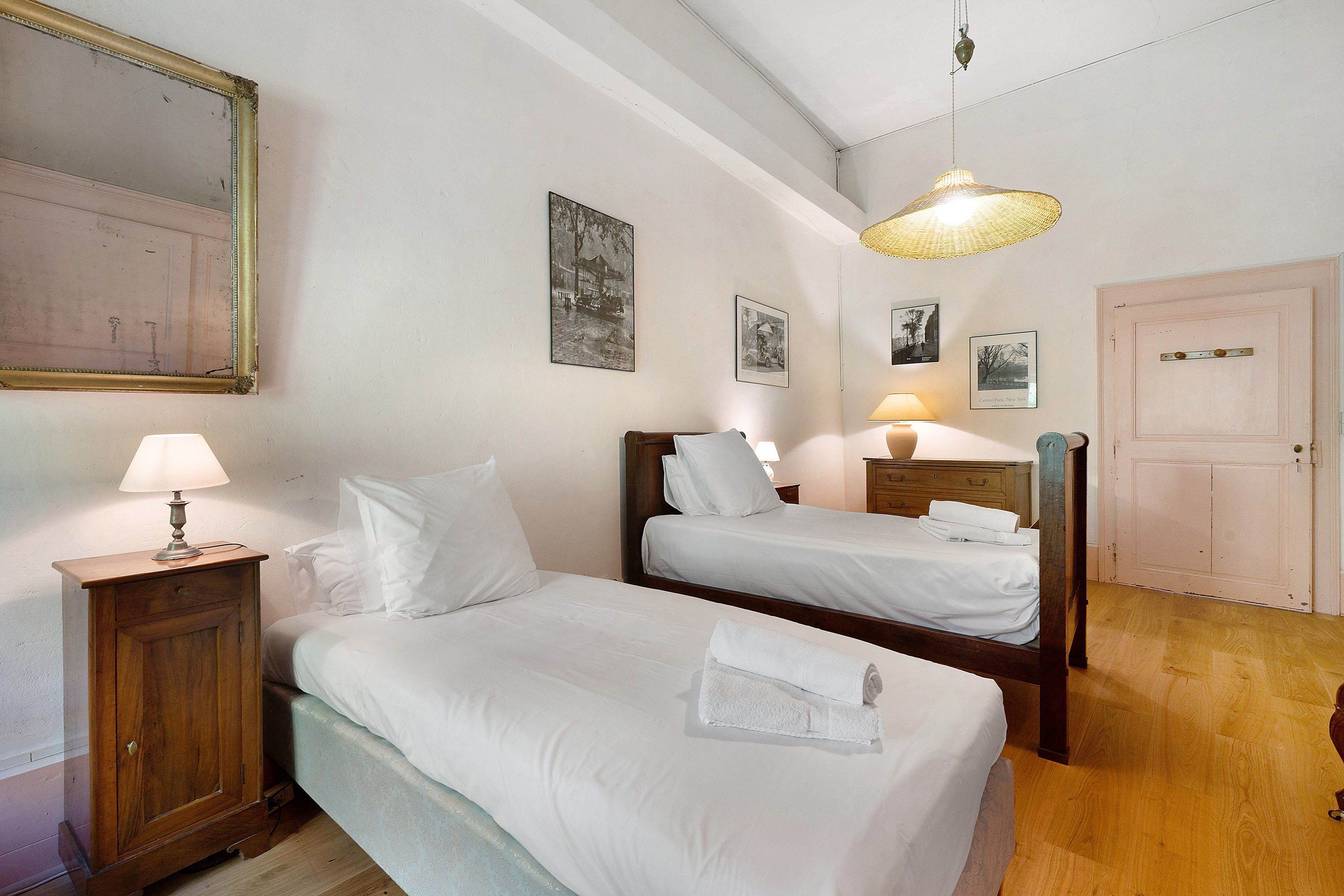 A hotel room with two single beds, a wooden wardrobe, a mirror, and a hanging light fixture.
