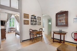 A room with a wooden floor, a dining table with chairs, a bookshelf, and a large mirror on the wall. - Château with Private Park – Gîte du Tilleul – Exceptional Setting (Tournon)