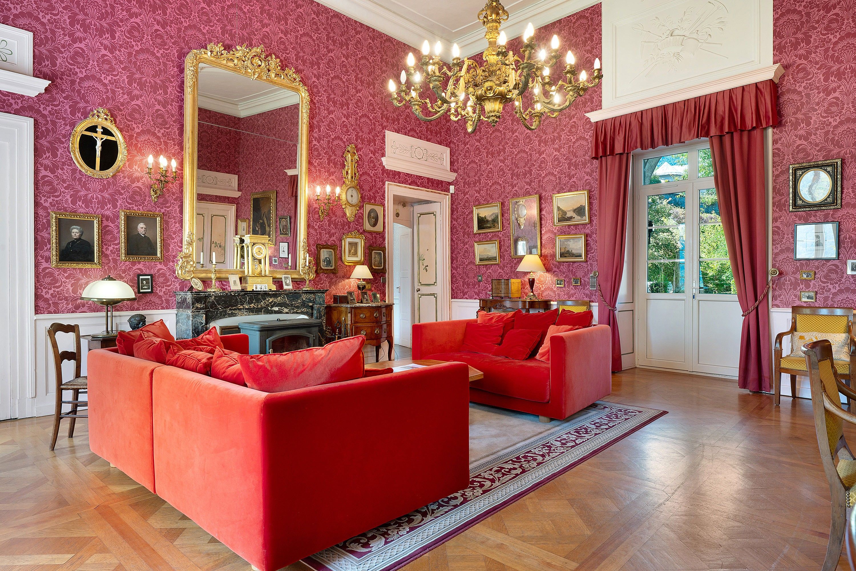 Une pièce dotée d’un grand miroir, de canapés rouges, d’un lustre et d’une cheminée.