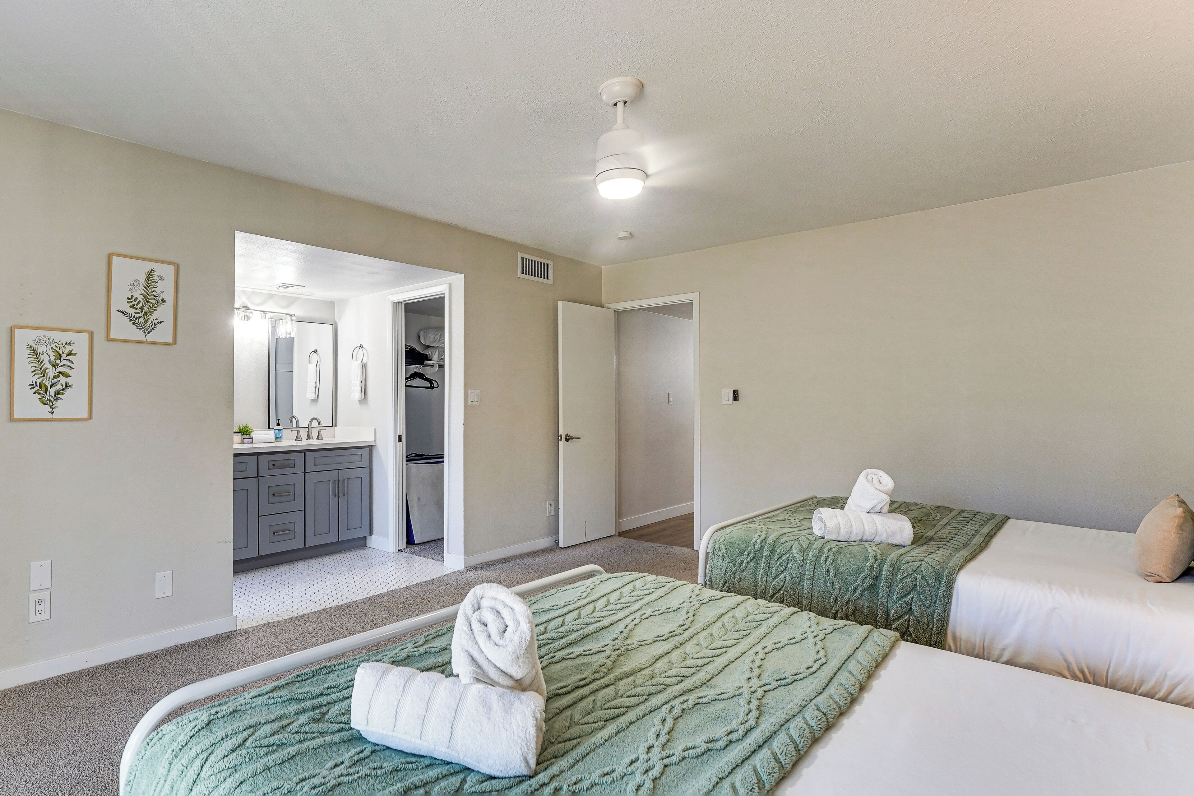 A hotel room with two beds, a bathroom with a sink and mirror, and a hallway leading to another room.
