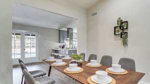 A dining area with a wooden table set for six, grey chairs, and a kitchen in the background. - Spacious Phoenix Oasis w/ Pool & Game Room (Phoenix)