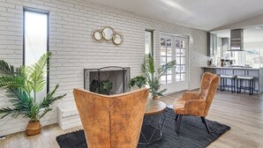 A modern living room with a fireplace, two armchairs, and a dining area with bar stools. - Spacious Phoenix Oasis w/ Pool & Game Room (Phoenix)