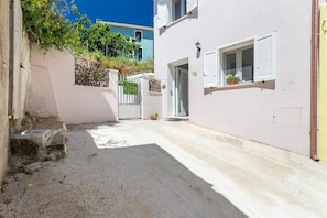 A narrow alleyway with a white building, a door, and a window with shutters.