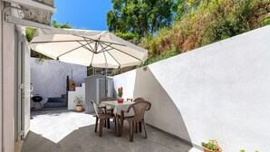 Eine Terrassenausstattung mit Tisch, Stühlen, einem großen Sonnenschirm und Kübelpflanzen.