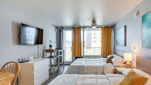 Une chambre d’hôtel équipée d’une télévision à écran plat, d’un bureau avec une chaise, de deux lits avec des oreillers, d’une table de chevet avec une lampe et d’une fenêtre avec des rideaux.